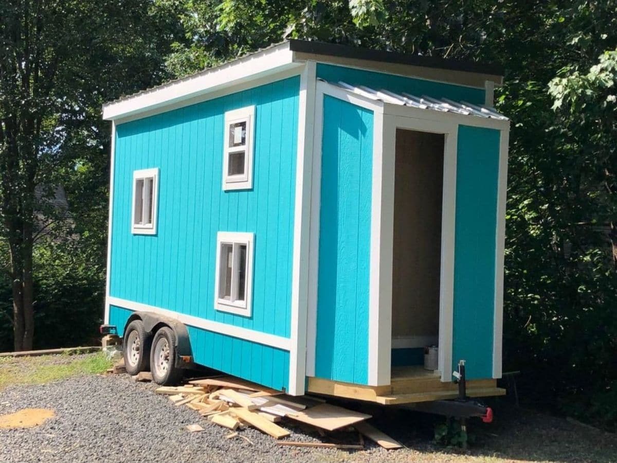 teal tiny home on wheels with white trim and three windows