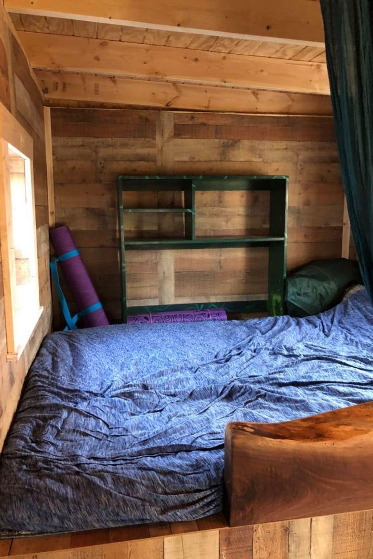 light blanket on bed in loft with green shelf against back wall