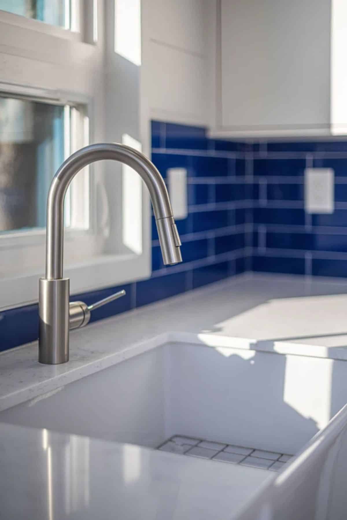 stainless steel faucet on white sink with blue tile background
